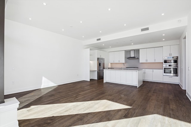 kitchen featuring white cabinets, wood-type flooring, a kitchen island with sink, and wall chimney exhaust hood