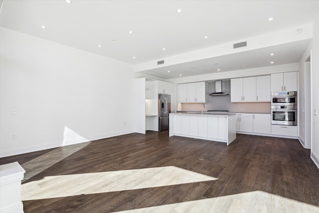 kitchen featuring white cabinetry, wall chimney exhaust hood, hardwood / wood-style floors, an island with sink, and appliances with stainless steel finishes