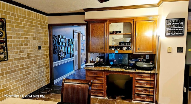 kitchen featuring a textured ceiling, crown molding, built in desk, and light stone countertops