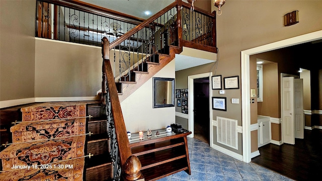 stairway featuring stone finish flooring, visible vents, baseboards, and a high ceiling