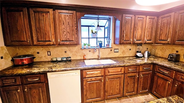 kitchen with white dishwasher, backsplash, dark stone counters, and sink