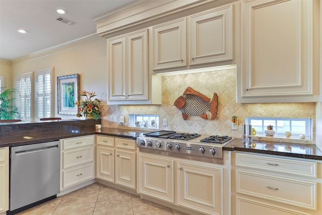 kitchen with stainless steel appliances, cream cabinets, a wealth of natural light, light tile patterned floors, and ornamental molding