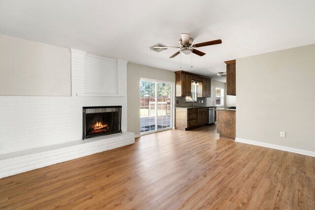 unfurnished living room featuring a brick fireplace, light hardwood / wood-style flooring, ceiling fan, and sink