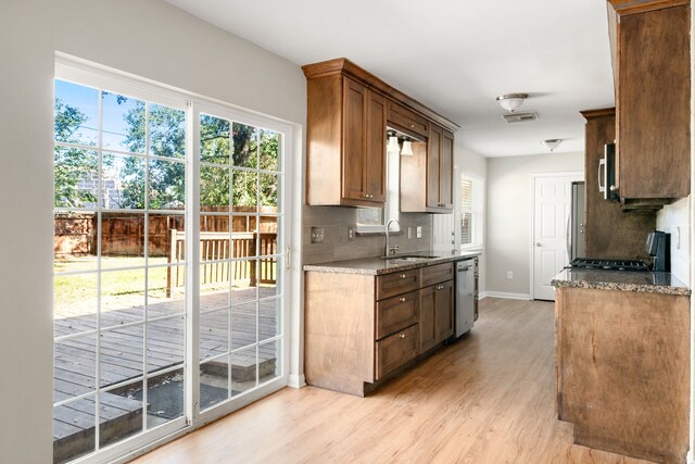 kitchen with light stone countertops, sink, stainless steel appliances, tasteful backsplash, and light hardwood / wood-style flooring