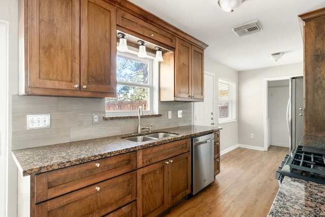 kitchen featuring backsplash, dark stone counters, sink, light hardwood / wood-style flooring, and appliances with stainless steel finishes