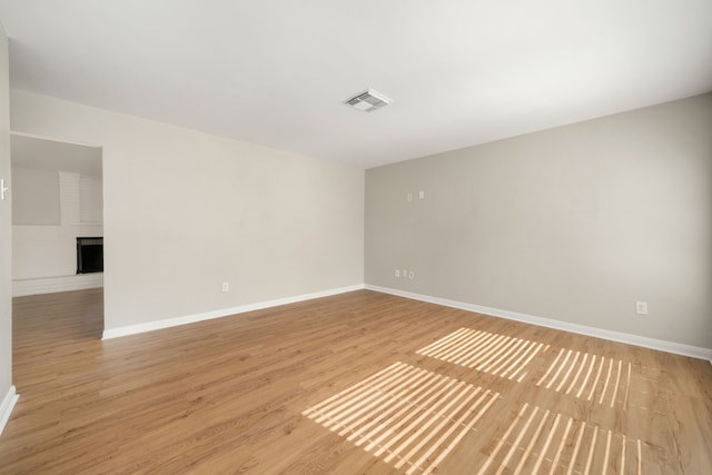 empty room with light hardwood / wood-style floors and a brick fireplace