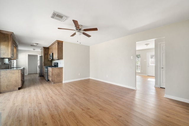 unfurnished living room featuring light wood-type flooring, ceiling fan, and sink