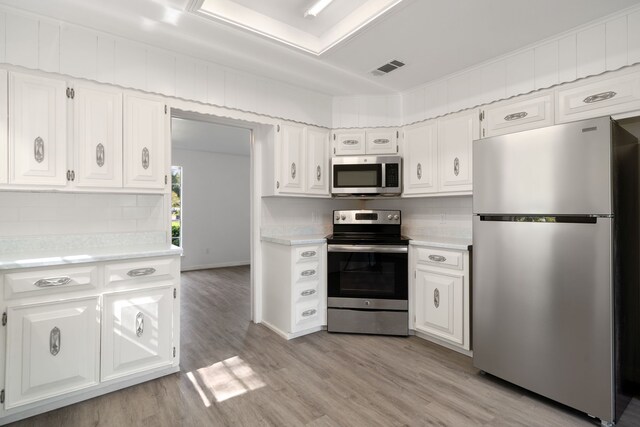 kitchen with light hardwood / wood-style floors, white cabinetry, decorative backsplash, and appliances with stainless steel finishes