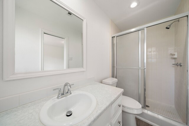 bathroom with toilet, vanity, and a shower with door