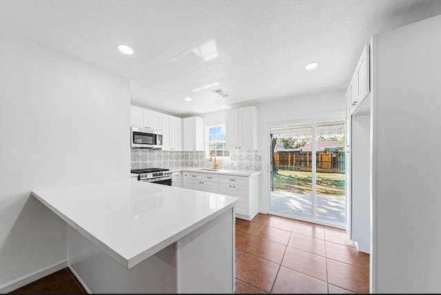 kitchen featuring sink, kitchen peninsula, decorative backsplash, appliances with stainless steel finishes, and white cabinetry