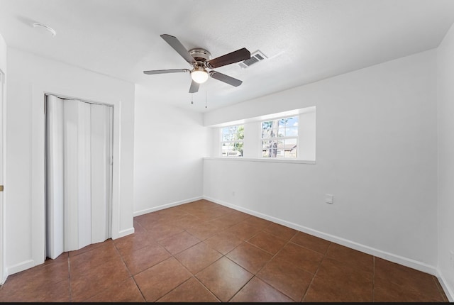 unfurnished bedroom with a closet, dark tile patterned flooring, and ceiling fan