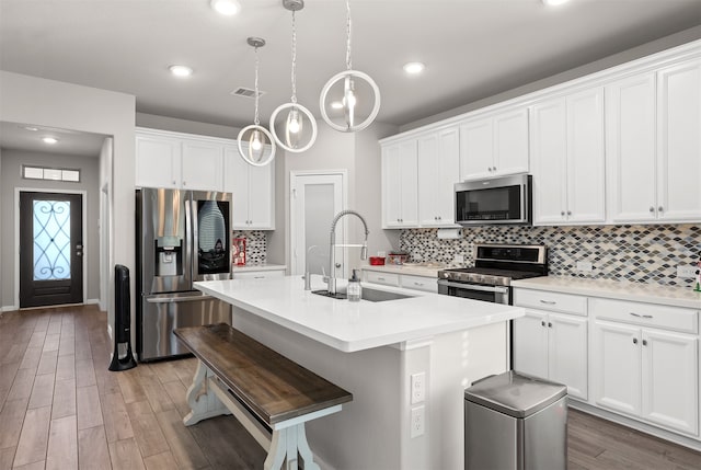 kitchen with hanging light fixtures, sink, appliances with stainless steel finishes, and an island with sink