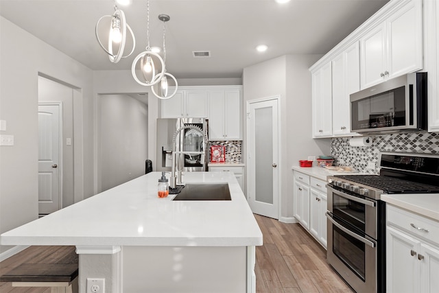 kitchen featuring stainless steel appliances, backsplash, an island with sink, light hardwood / wood-style floors, and white cabinets