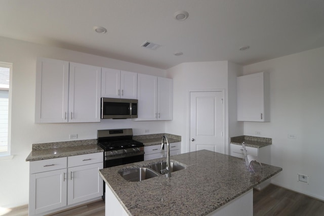 kitchen with white cabinets, a center island with sink, sink, dark stone countertops, and stainless steel appliances