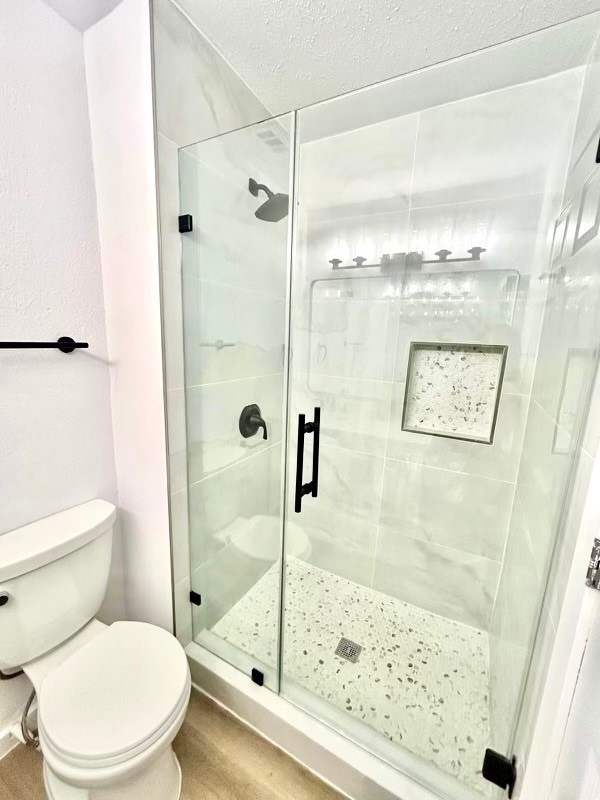 bathroom featuring hardwood / wood-style flooring, a textured ceiling, toilet, and an enclosed shower