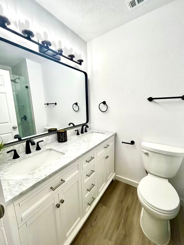 bathroom featuring toilet, hardwood / wood-style floors, a textured ceiling, an enclosed shower, and vanity