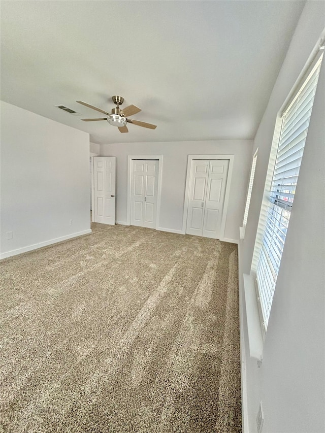 unfurnished bedroom with carpet, multiple closets, and ceiling fan