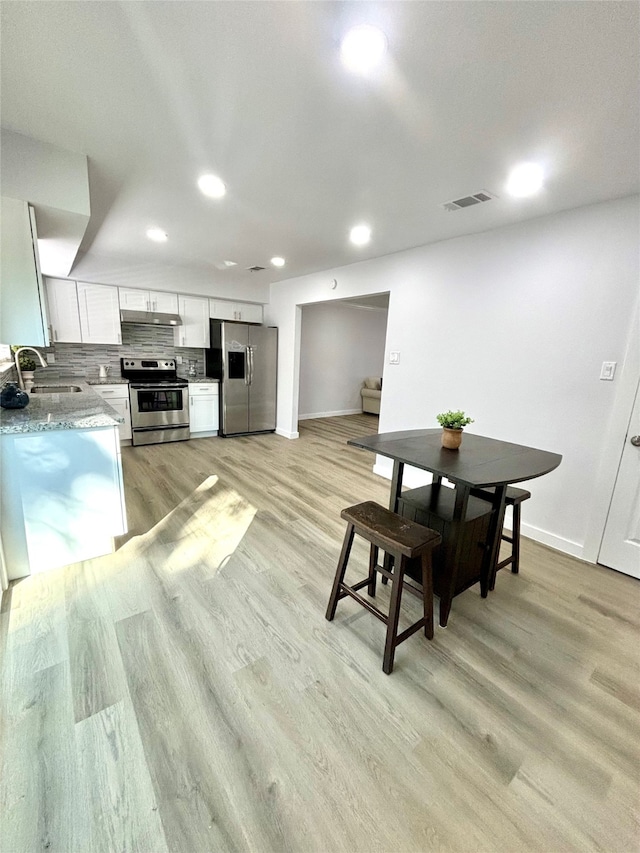 kitchen featuring light stone counters, light wood-type flooring, appliances with stainless steel finishes, sink, and white cabinets