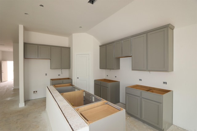 kitchen with lofted ceiling, unfinished concrete flooring, a kitchen island, and gray cabinetry