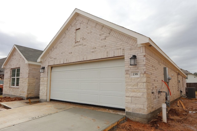 view of property exterior with brick siding, central air condition unit, a garage, and roof with shingles