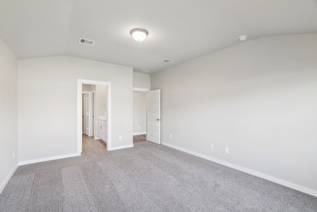 unfurnished bedroom with lofted ceiling, light carpet, and connected bathroom