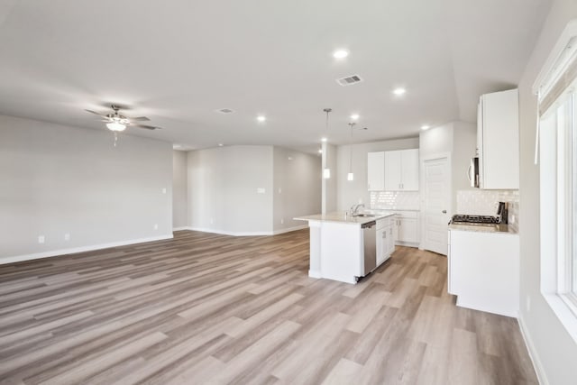 kitchen featuring pendant lighting, stainless steel appliances, white cabinets, a center island with sink, and decorative backsplash