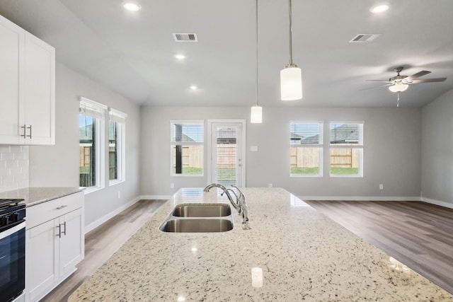 kitchen with white cabinetry, sink, pendant lighting, and light stone counters