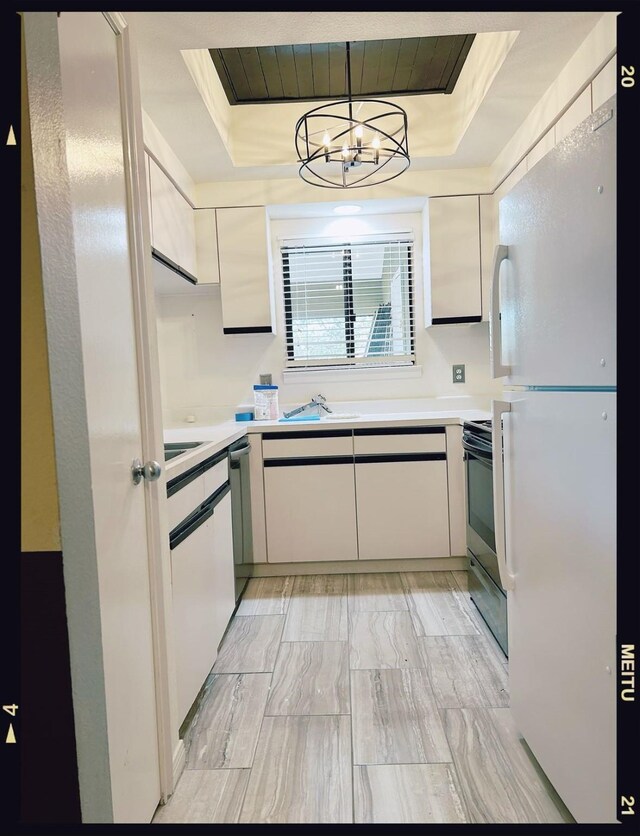 kitchen featuring a raised ceiling, appliances with stainless steel finishes, pendant lighting, and an inviting chandelier