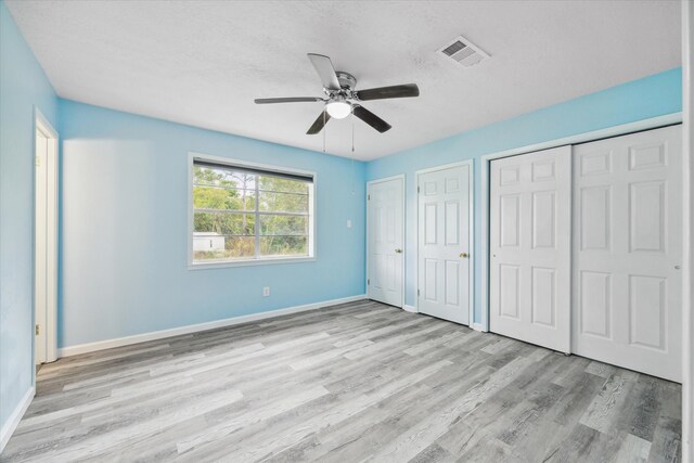 unfurnished bedroom with a textured ceiling, ceiling fan, two closets, and light wood-type flooring