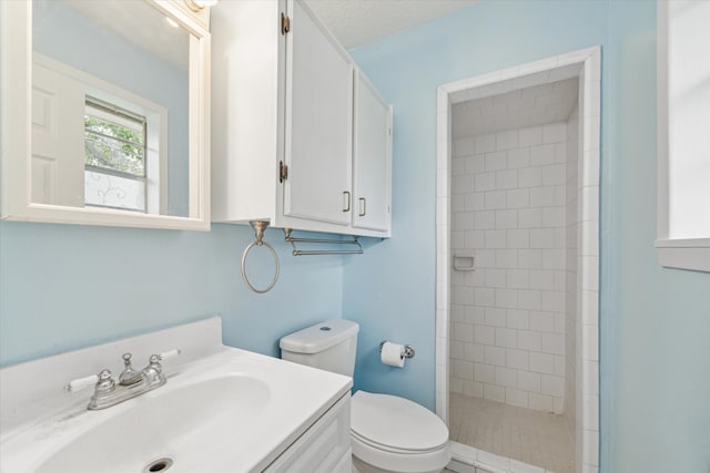 bathroom with toilet, vanity, and tiled shower