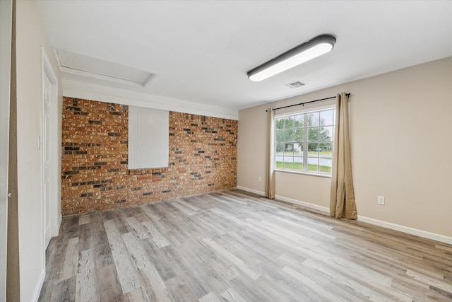 spare room with light wood-type flooring and brick wall