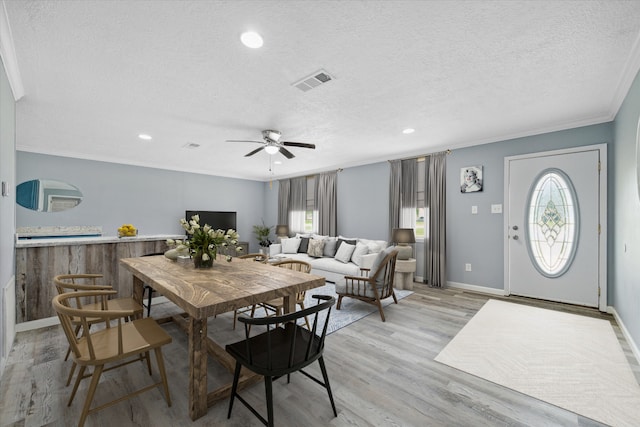 dining space with light hardwood / wood-style flooring, a healthy amount of sunlight, a textured ceiling, and ornamental molding