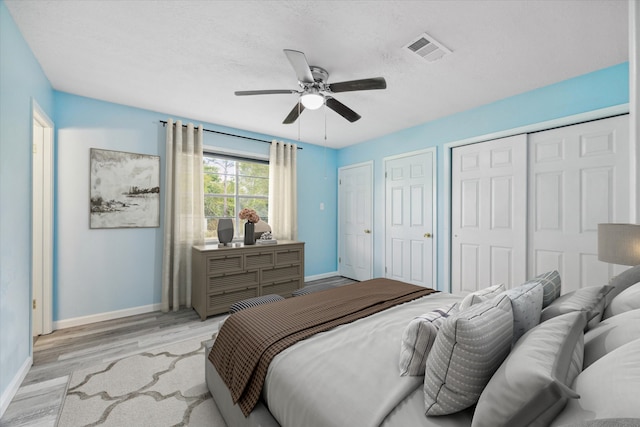 bedroom with a textured ceiling, ceiling fan, light hardwood / wood-style flooring, and two closets