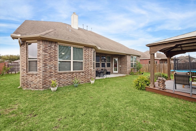 rear view of property with a trampoline, a gazebo, a yard, a patio area, and a deck