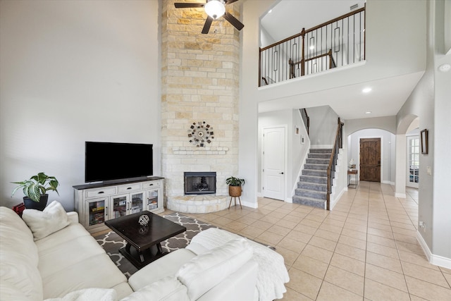 tiled living room featuring ceiling fan, a stone fireplace, and high vaulted ceiling