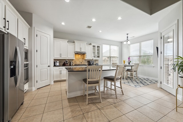 kitchen featuring a center island, light tile patterned floors, decorative backsplash, white cabinets, and appliances with stainless steel finishes