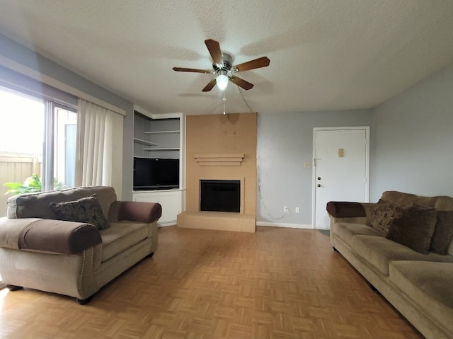 living room with ceiling fan, a textured ceiling, a fireplace, light parquet floors, and built in features