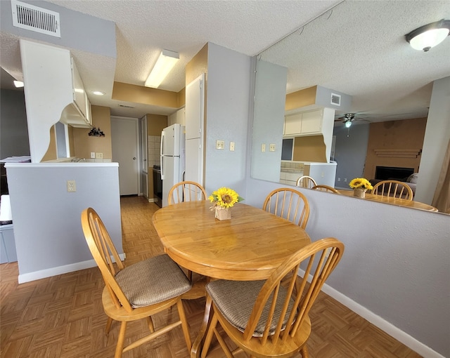 dining room featuring dark parquet flooring, ceiling fan, a textured ceiling, and a large fireplace