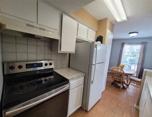 kitchen featuring tile counters, white refrigerator, white cabinets, stainless steel range with electric stovetop, and extractor fan