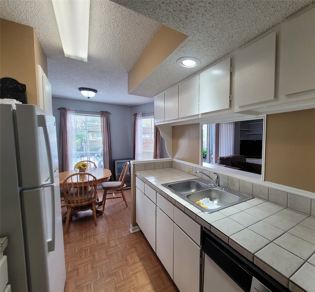 kitchen with tile counters, sink, white refrigerator, and white cabinets