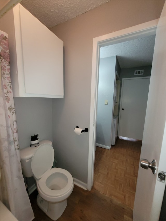 bathroom with parquet floors, a textured ceiling, and toilet