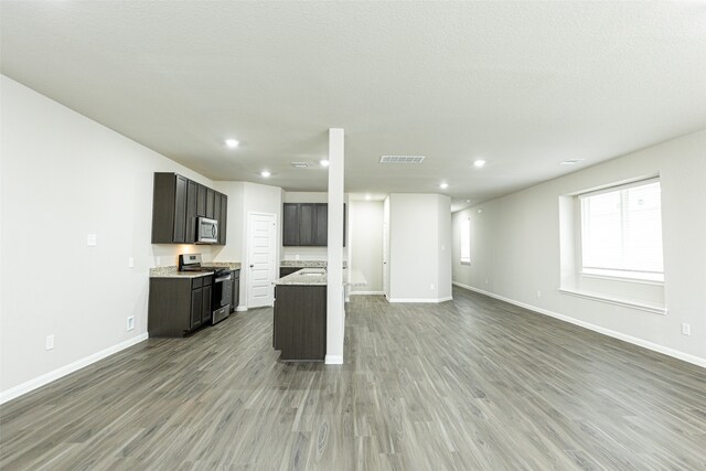 kitchen with a textured ceiling, appliances with stainless steel finishes, hardwood / wood-style flooring, and light stone counters