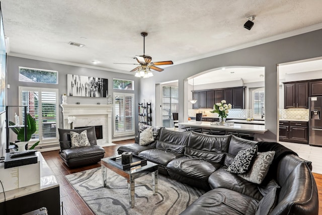 living room featuring ceiling fan, a premium fireplace, crown molding, a textured ceiling, and hardwood / wood-style flooring