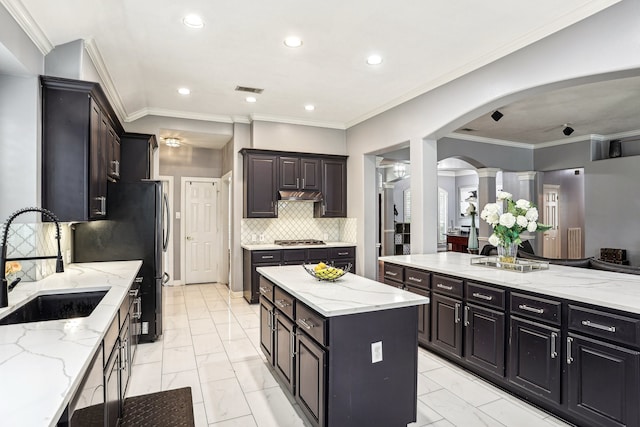 kitchen with ornate columns, crown molding, sink, and a center island