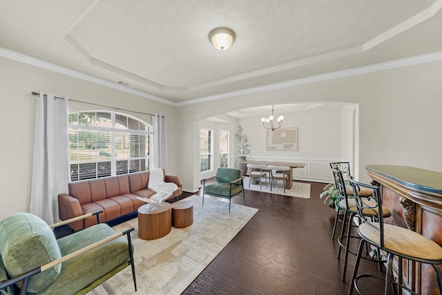 living room with a raised ceiling, dark hardwood / wood-style flooring, ornamental molding, and an inviting chandelier