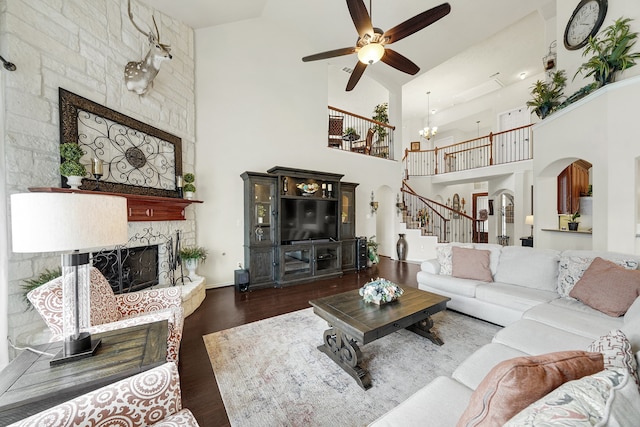 living room with ceiling fan with notable chandelier, dark hardwood / wood-style floors, high vaulted ceiling, and a stone fireplace