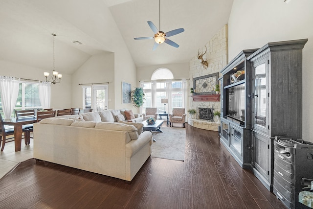 living room featuring dark hardwood / wood-style floors, a stone fireplace, ceiling fan with notable chandelier, and high vaulted ceiling