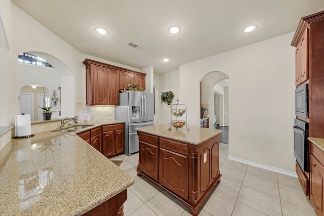 kitchen with sink, stainless steel appliances, light tile patterned floors, light stone counters, and a kitchen island