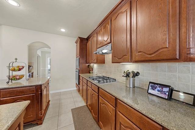 kitchen featuring decorative backsplash, light tile patterned floors, light stone countertops, and appliances with stainless steel finishes