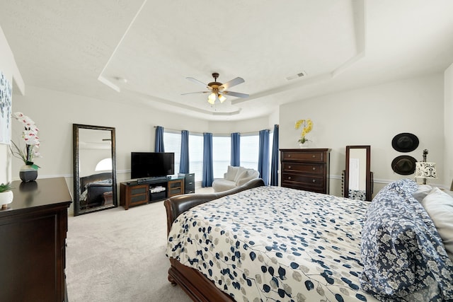 bedroom with light carpet, a raised ceiling, and ceiling fan